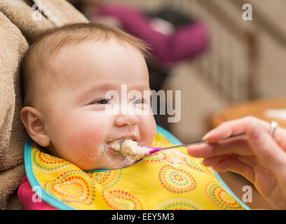 Small baby girl is given her first solid food on a spoon and is unsure about the process Stock Photo