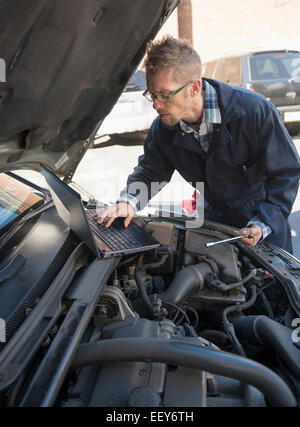 Mechanic using laptop while repairing car Stock Photo