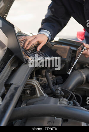 Mechanic using laptop while repairing car Stock Photo