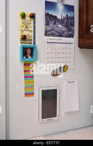 Magnet notes, calendar, lottery ticket, and web internet connectivity tablet screen on side of a refrigerator Stock Photo