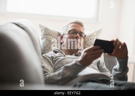 Man lying on sofa using phone Stock Photo
