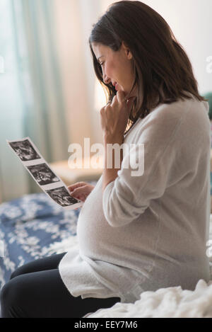 Pregnant woman watching ultrasound, sitting on bed Stock Photo