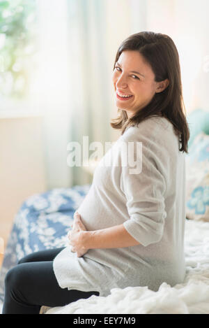 Pregnant woman holding ultrasound, sitting on bed smiling Stock Photo