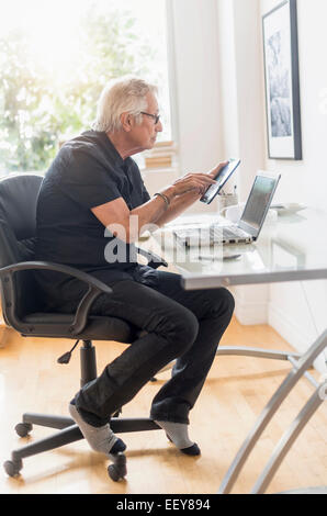 Senior man sitting in home office, using tablet pc Stock Photo