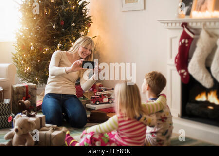 Mother with children (4-5, 6-7) opening christmas presents and taking photos Stock Photo