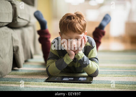 Boy (6-7) lying on carpet and using tablet pc Stock Photo