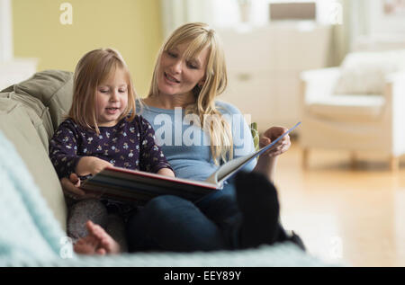 Mother and daughter (4-5) sitting on couch and reading book Stock Photo