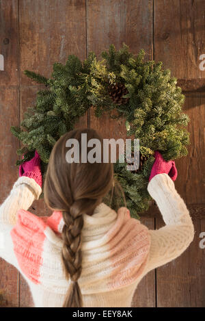 Young woman hanging christmas wreath on door Stock Photo