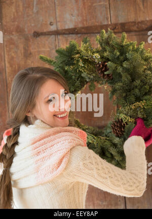 Portrait of young woman hanging christmas wreath on door Stock Photo