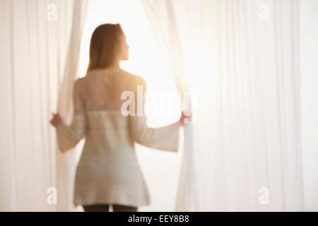 Young woman opening curtains in morning Stock Photo