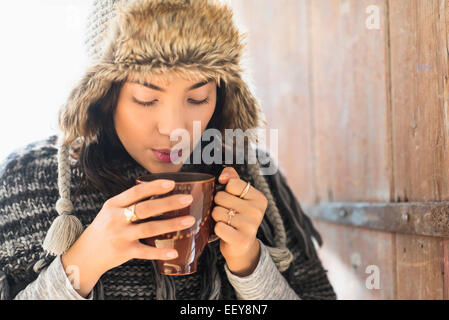 Portrait of young woman wearing warm hat, blowing on cup of drink Stock Photo