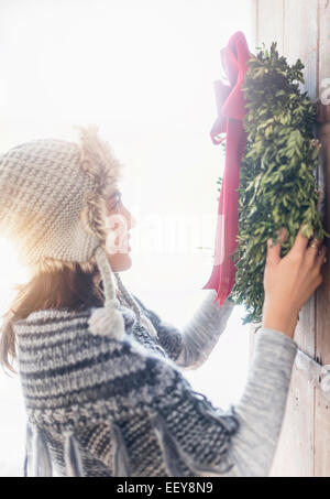 Side view of young woman hanging Christmas wreath on entrance door Stock Photo