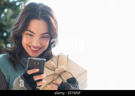 Smiling young woman holding gift and text messaging Stock Photo