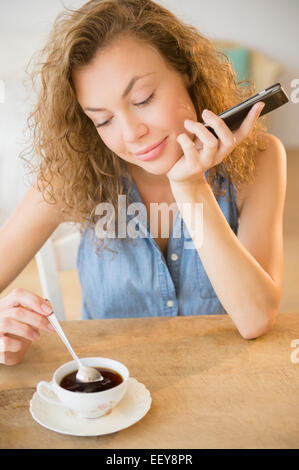 Young woman holding smart phone and stirring tea Stock Photo
