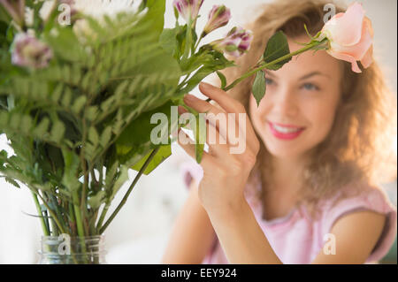 Smiling young woman putting flowers in vase Stock Photo