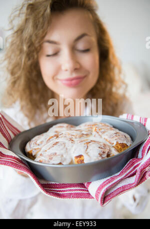Young woman with eyes closed holding fresh cinnamon rolls Stock Photo