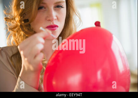 Portrait of young woman popping balloon Stock Photo