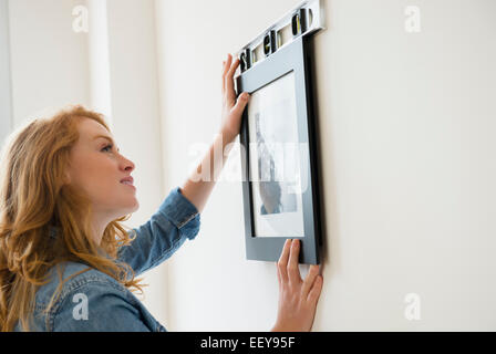 Woman hanging picture on wall Stock Photo
