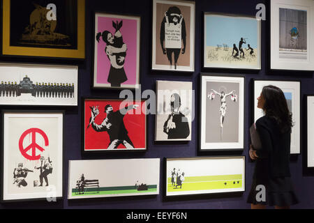 London, UK. 23 January 2015. A Bonhams employee looks at the Banksy prints from the Steve Lazarides collection. Included among the collection of iconic prints are Flower Thrower (2003), Rude Copper (2002), and Christ With Shopping Bags (2004), each estimated at £8,000-12,000. Bonhams auction house previews items from the 'Founded 1793' contemporary art auction taking place on 28 January 2015. The sale includes a collection of 30 Banksy prints owned by the English gallery owner, Steve Lazarides, and a ukulele decorated by Damien Hurst. Photo: Bettina Strenske Stock Photo