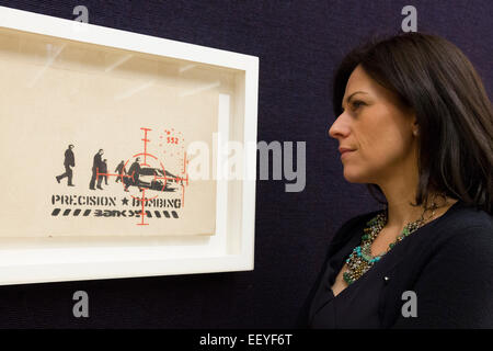 London, UK. 23 January 2015. A Bonhams employee poses with the Banksy picture 'Precision Bombing'. Bonhams auction house previews items from the 'Founded 1793' contemporary art auction taking place on 28 January 2015. The sale includes a collection of 30 Banksy prints owned by the English gallery owner, Steve Lazarides, and a ukulele decorated by Damien Hurst. Photo: Bettina Strenske Stock Photo