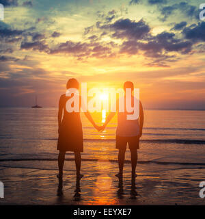 Silhouette of a young couple on their honeymoon standing on the ocean beach at amazing sunset. Stock Photo