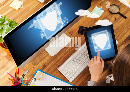Woman working with tablet and pc placed on wooden desk with digital scheme of security. Shot from aerial view Stock Photo