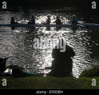 A rowing team passes a fisherman silhouetted by winter sunshine on the River Severn in Shrewsbury, Shropshire. Stock Photo