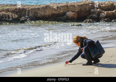 Calpe, Spain, woman writing in the sand on the beach with stick holding a bag Stock Photo