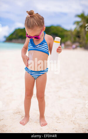 Little cute adorable girl in swimsuit rubs sunscreen herself Stock Photo