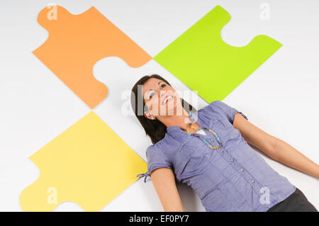 Woman lying on floor beside oversized puzzle pieces Stock Photo