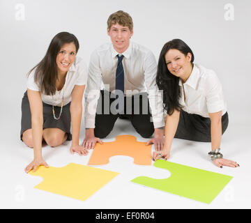 Three people sitting on floor looking at puzzle pieces Stock Photo