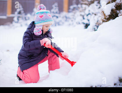 Little adorable girl play with snow shoveling on winter day Stock Photo