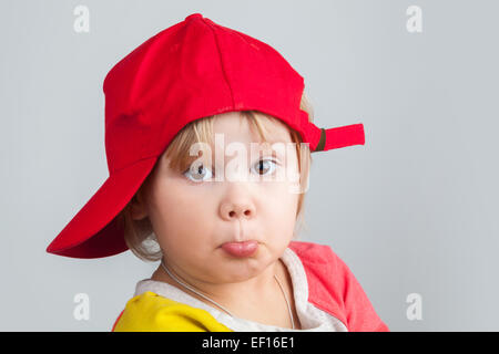 Studio portrait of funny confused baby girl in red baseball cap over gray wall background Stock Photo
