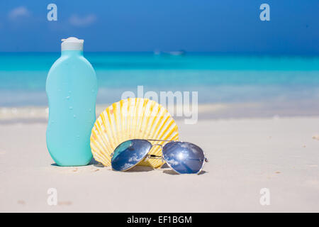 Bottle of suncream, sunglasses and shell on the white beach Stock Photo