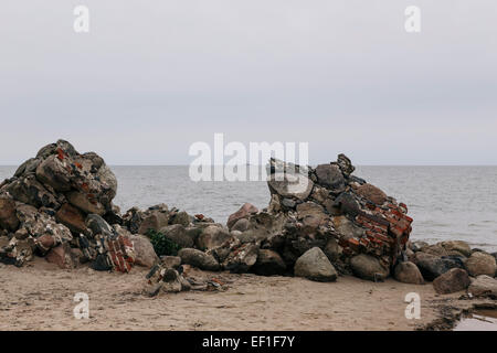 Rocks and broken bricks from remains of demolished lighthouse at point of Cape Kolka with lighthouse in distance Stock Photo
