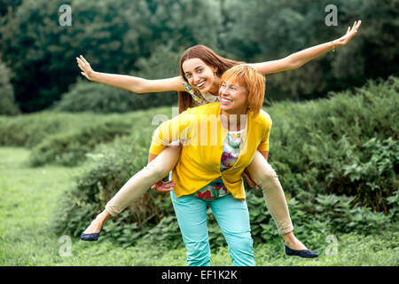 Mother giving piggyback riding to her daughter in the park Stock Photo