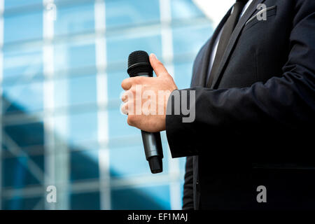 Man holding microphone in the hand on blue contempopary background Stock Photo