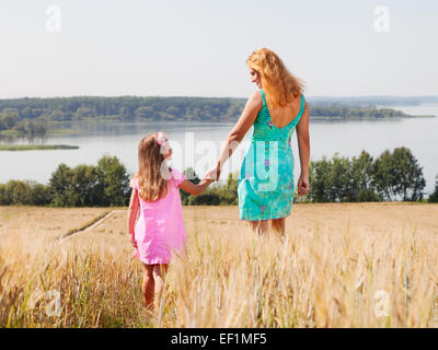 Mother and daughter walking  in summer field near lake on a sunny day Stock Photo