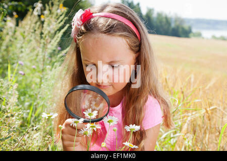 Little girl exploring the daisy flower through the magnifying glass outdoors Stock Photo