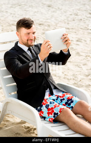 Businessman taking selfie photo with digital tablet sitting on the sunbed on the beach Stock Photo