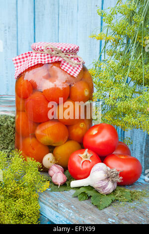 Homemade pickled tomatoes in glass jar. Fresh vegetables, dill and garlic on wooden board Stock Photo