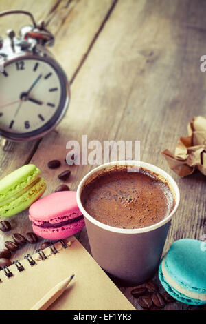 macaroons, espresso coffee cup, sketch book and alarm clock on wooden rustic table, vintage stylized photo Stock Photo