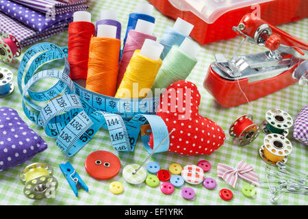 Tailor items: spools of colorful thread, buttons, fabrics, measuring tape, pincushion, small sewing machine and measuring tape Stock Photo