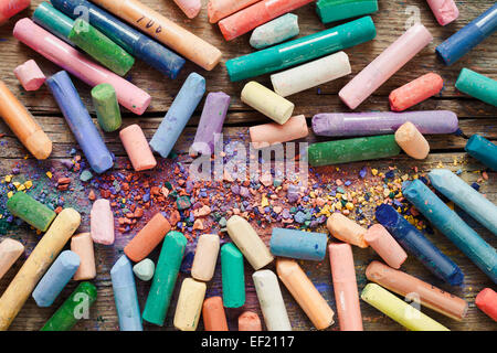 Collection of rainbow colored pastel crayons with pigment dust on old desk. Stock Photo