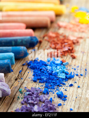Collection of rainbow colored pastel crayons with crushed chalk on old wooden desk. Stock Photo