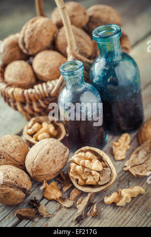 Walnuts in basket and nuts tincture or oil on old wooden table Stock Photo