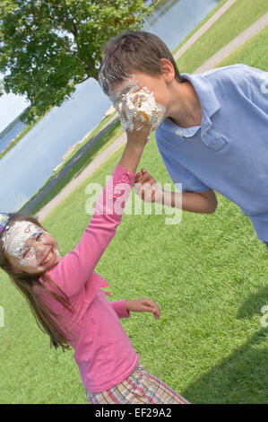 Girl putting cake on boy's face Stock Photo