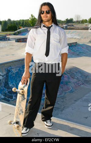A young man in a shirt and tie holding a skateboard Stock Photo