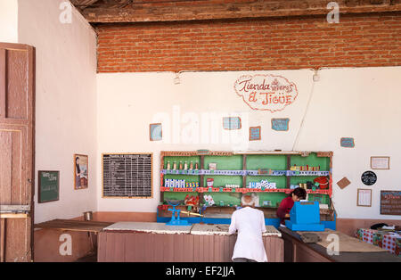 Cuban lifestyle: Local man buying from a sparsely stocked general store shop in Trinidad, Cuba, old fashioned till and scales on counter Stock Photo
