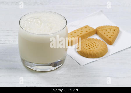 Close up shot of a glass of freshly poured milk with cookies in the background on white wooden table. Stock Photo